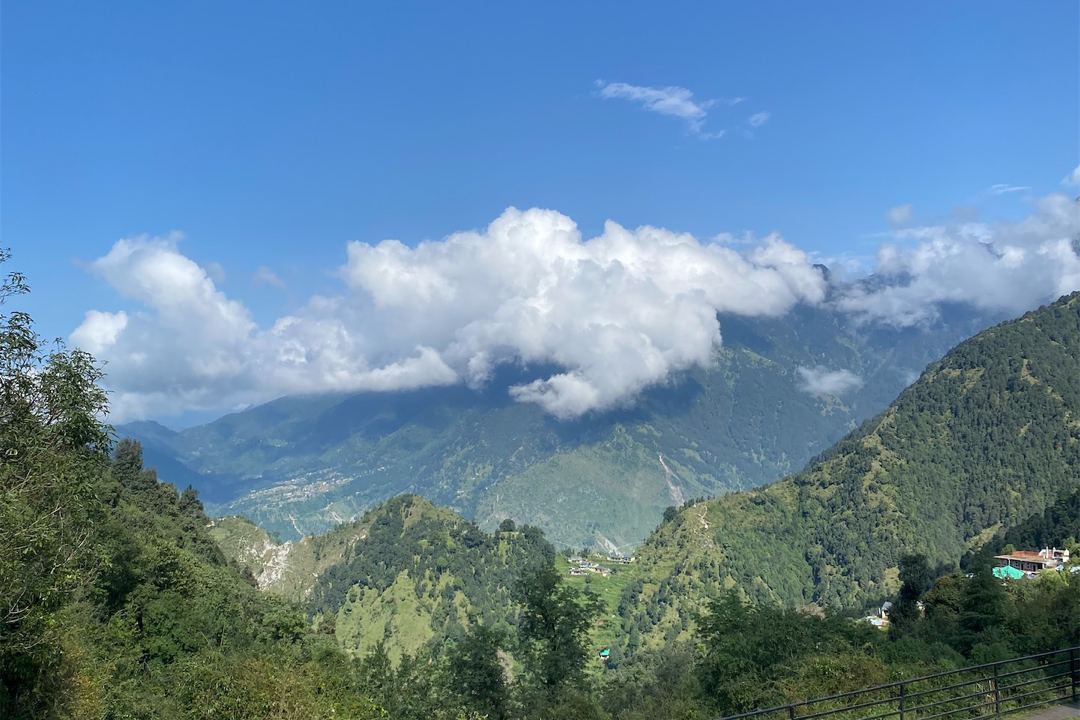 Green mountains under white clouds and a blue sky, with a deep valley below